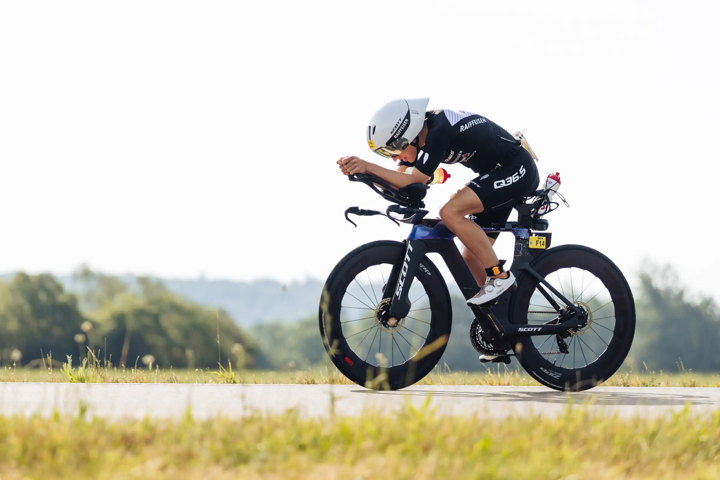 Loanne Duvoisin racing on a time trial bike, tucked low on the aero bars on an open road, wearing an aero helmet and a race number