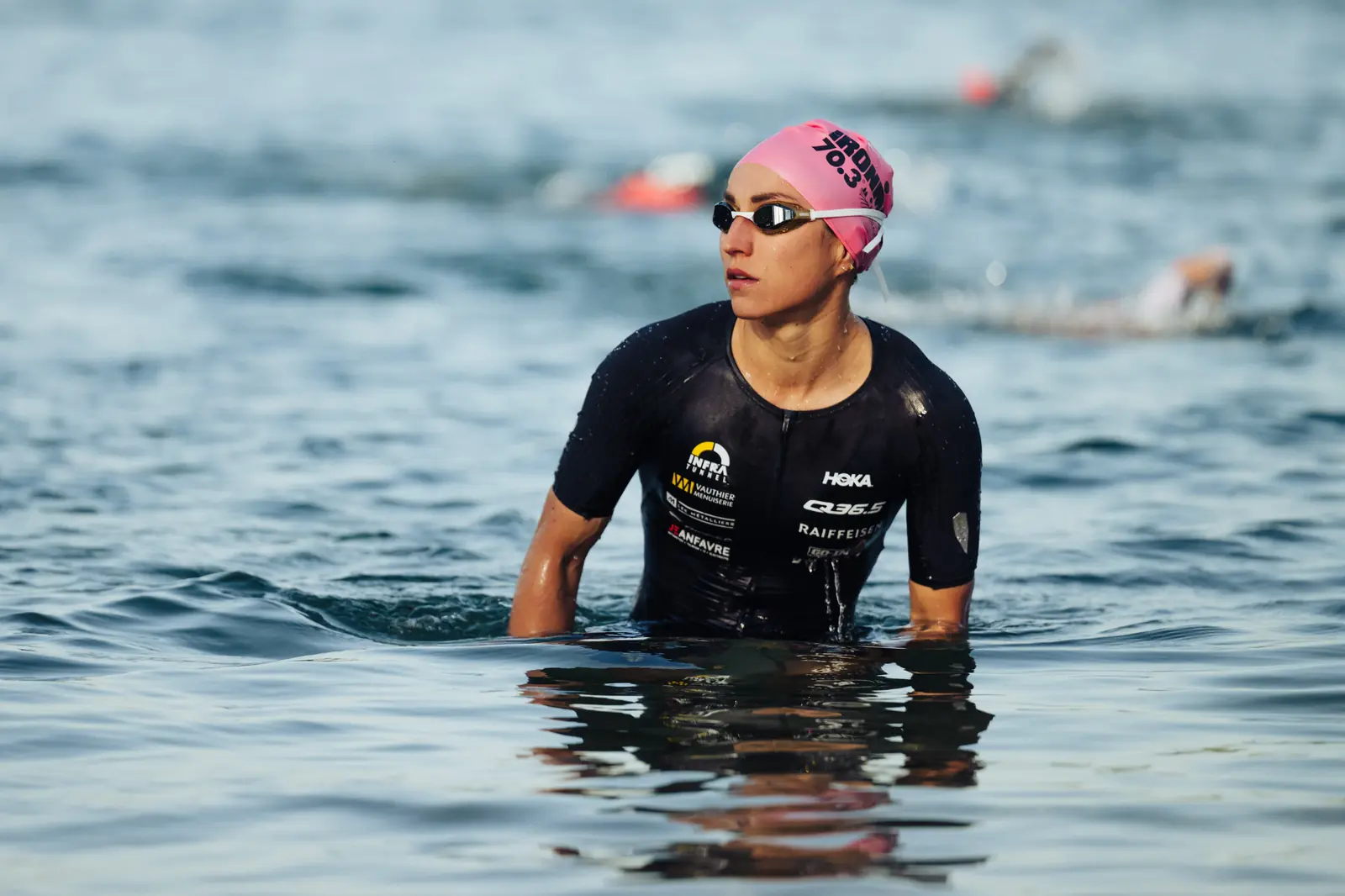 Loanne Duvoisin chest-deep in open water before a race start, in a pink swim cap and goggles